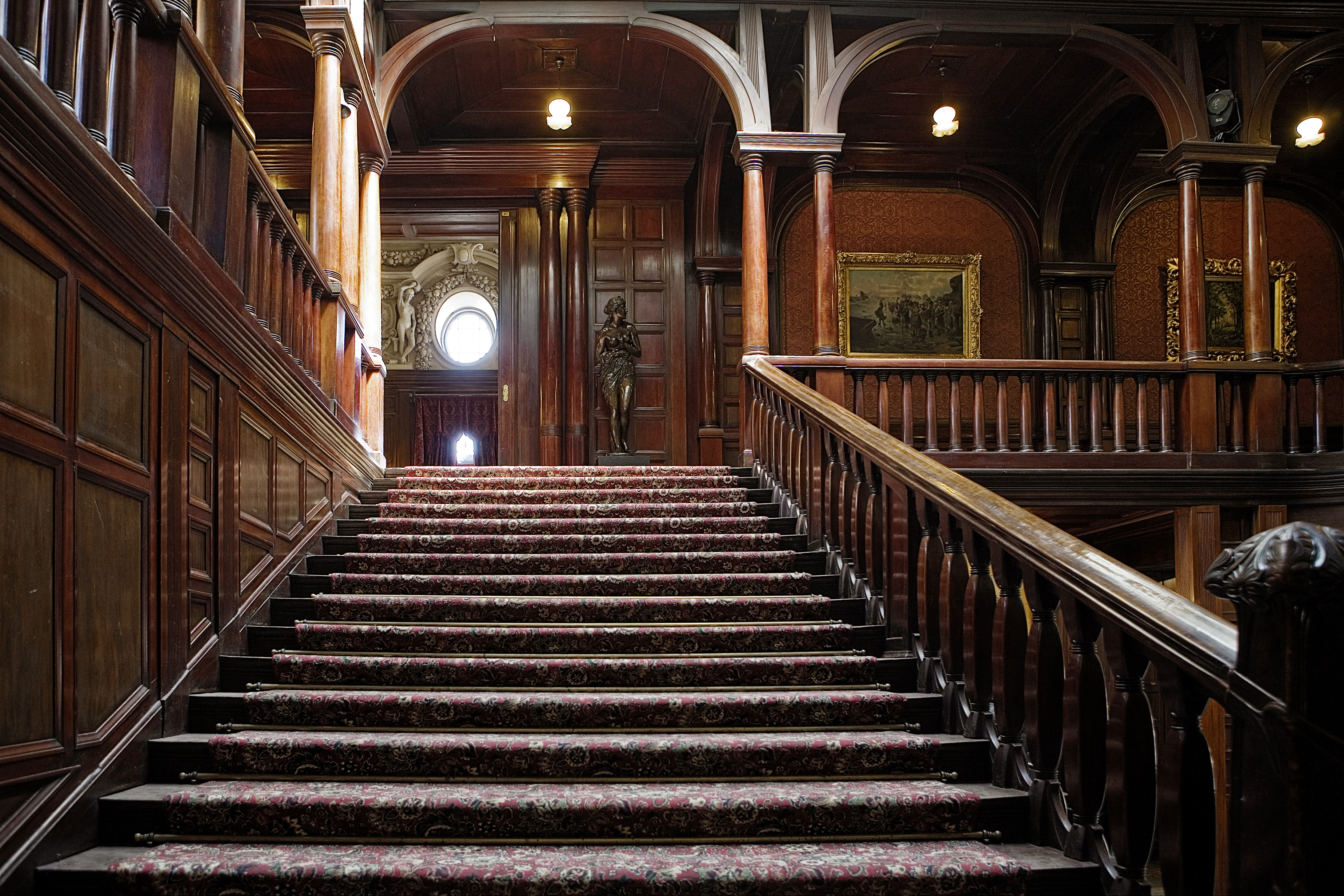 Widok na drewniane schody prowadzace na poziom reprezentacyjnych sal pałacu i drewniane dekoracje klatki schodowej.