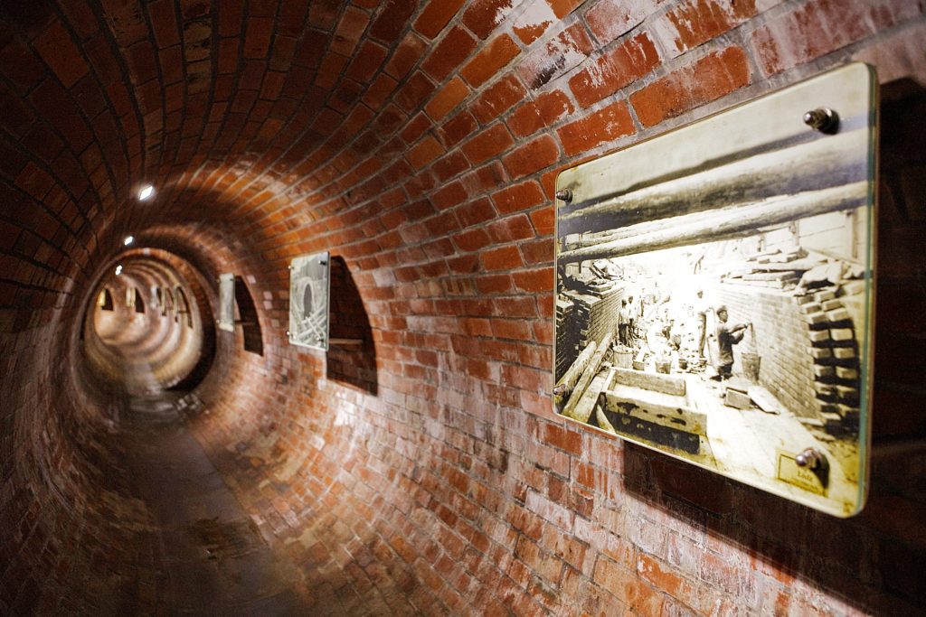 Widok w głąb korytarza Dętki, podziemnego zbiornika na wodę deszczową, obecnie udostępnionego do zwiedzania, wraz z kolekcją dawnych zdjęć z okresu budowy sieci kanałów.