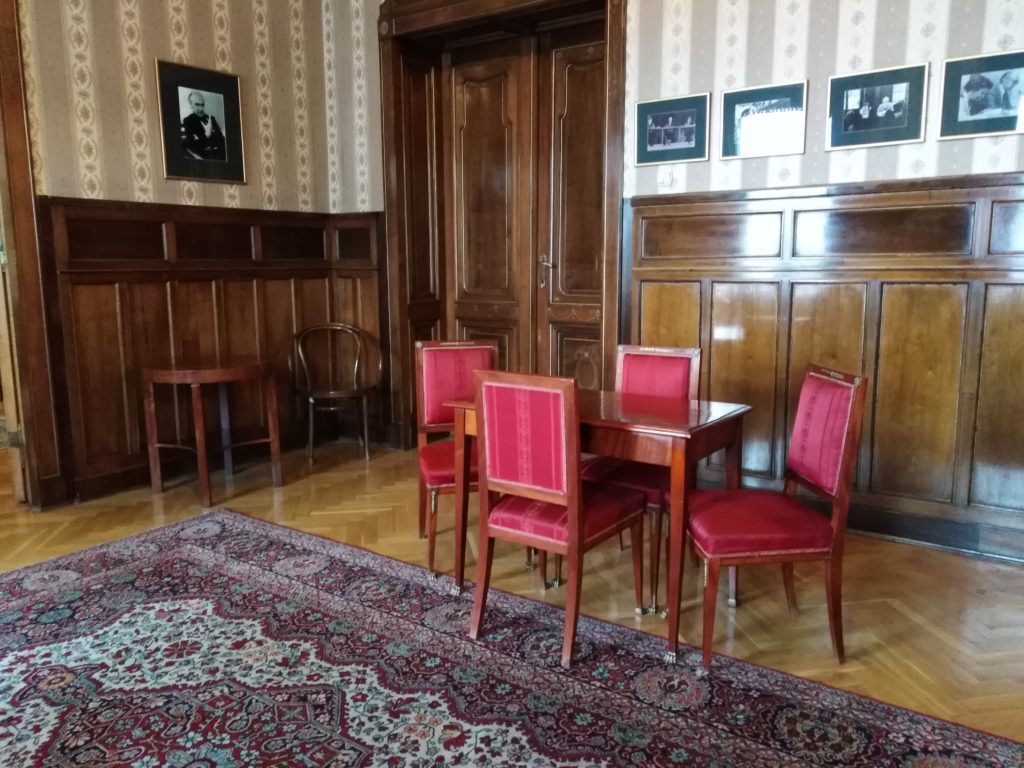 Widok gabinetu Karla Dedeciusa z kompletem czerwono tapicerwanych krzeseł i stolikiem drewnianym na pierwszym planie.