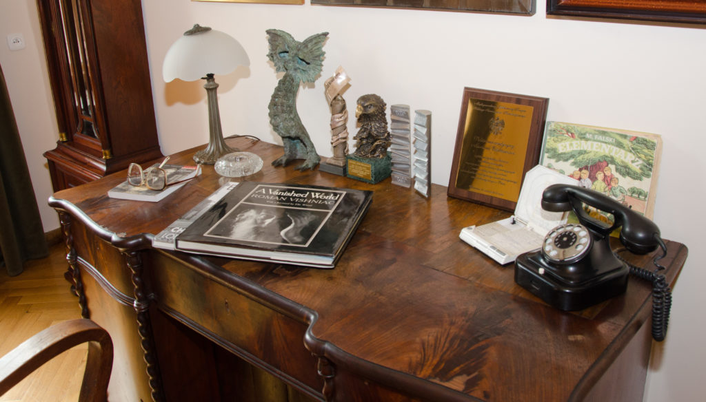Widok na biurko Marka Edelmana, na którym znajdują się osobiste pamiątki, odznaczenia, książki i telefon w bakelitowej obudowie.