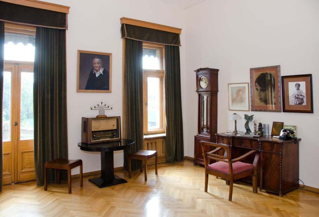 Widok na gabinet Marka Edelmana, z biurkiem i lampowym aparatem radiowym z pierwszej połowy dwudziestego wieku, umieszczonym na okrągłym stoliku.