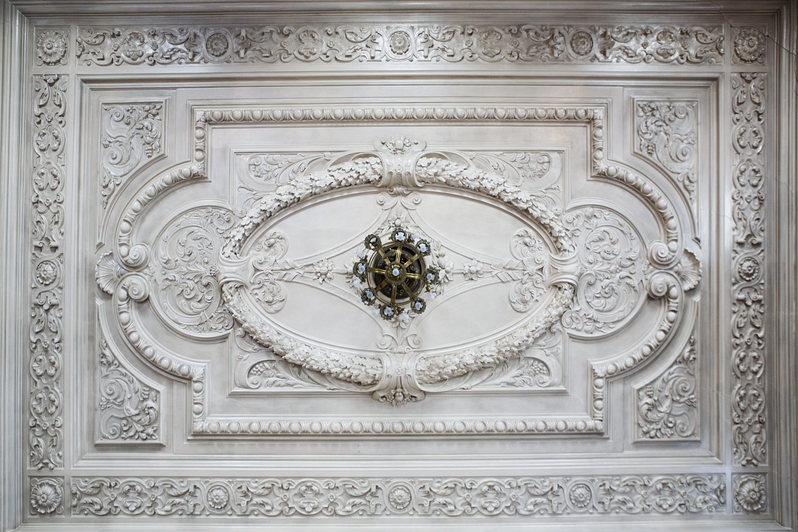 Widok na sztukaterię sufitu wielkiej sali jadalnej z jednym z żyrandoli elektrycznych.